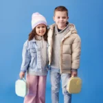 Dwoje dzieci trzymających mini śniadaniówki w kolorze miętowym i żółtym na niebieskim tle. b.box Mini Lunchbox Spearmint