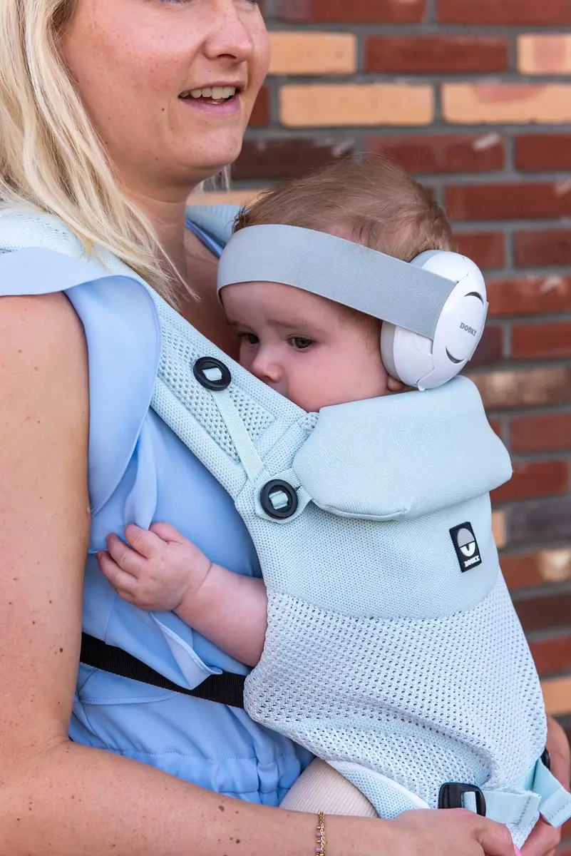 Biało-szare słuchawki ochronne dla niemowlaka na uszach dziecka noszonego w nosidełku dla mamy. Dooky Słuchawki ochronne Baby Earmuff white 0-3 l