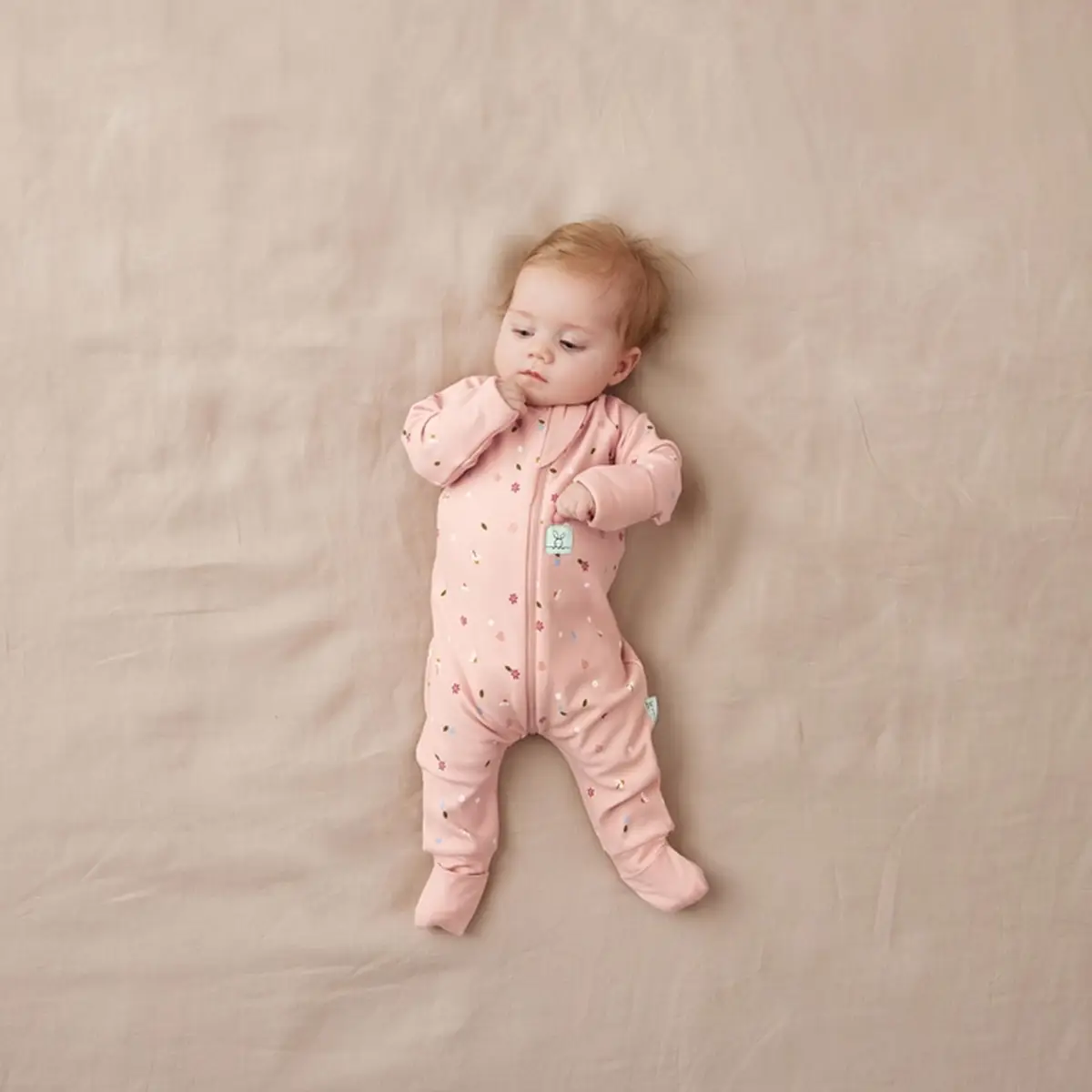 Niemowlę w różowym śpiworku z nogawkami w drobne kwiatki na jasnym tle dla dziecka 6-12 miesięcy. ergoPouch Śpiworek z nogawkami 1.0TOG Daisies 6-12M