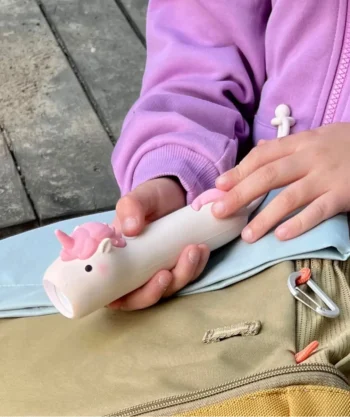 Latarka dziecięca w kształcie jednorożca w kolorze białym z różowymi elementami trzymana przez dziecko w różowej bluzie. Rabbit&Friends Latarka Jednorożec PINKY