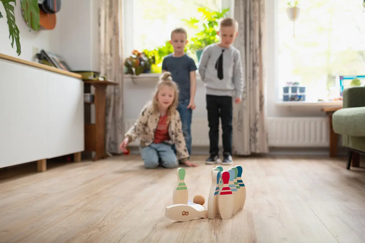 Drewniane kręgle z cyframi dla dzieci na podłodze w pokoju z trzema bawiącymi się dziećmi. BS Toys drewniane kręgle Cyferki