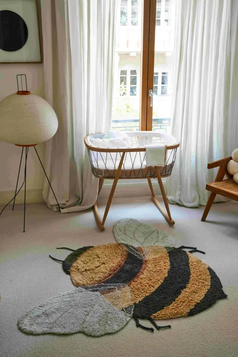 Bawełniany dywan w kształcie pszczoły w jasnym pokoju dziecięcym z kołyską i lampą stojącą dla niemowlaka. Lorena Canals Dywna bawełniany Bee do prania w pralce Planet Bee