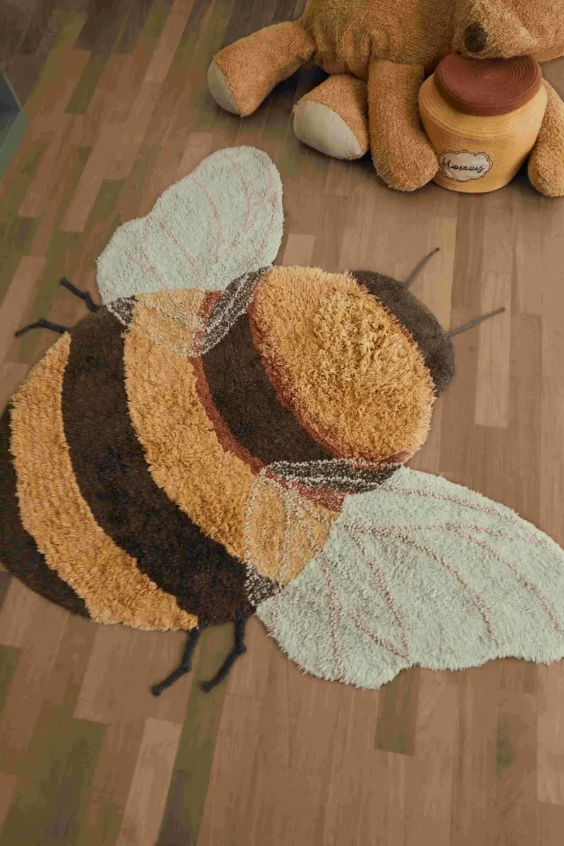 Bawełniany dywan dziecięcy w kształcie pszczoły w kolorach żółtym czarnym i białym na drewnianej podłodze. Lorena Canals Dywna bawełniany Bee do prania w pralce Planet Bee