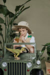 Chłopiec w kapeluszu trzymający butelkę obserwacyjną z dinozaurami siedząc na zielonym pojeździe zabawkowym z figurką dinozaura na masce. Petit Boum Butelka obserwacyjna dinozaury JURASSIC