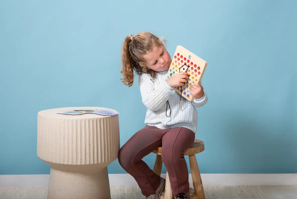 Dziewczynka bawiąca się drewnianą tablicą do kodowania z kolorowymi otworami i kartami pracy dla dzieci. BS Toys drewniana tablica do kodowania Przeplatanka z kartami pracy