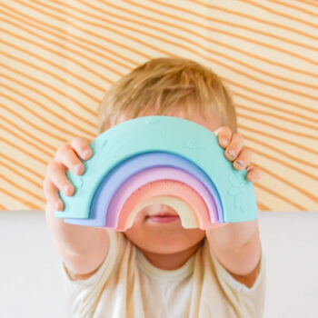 Pastelowa tęcza sensoryczna z pięciu elementów trzymana przez dziecko. Jellystone Designs Jellystone Tęcza sensoryczna Over the rainbow Pastel 5el. kolor pastelowy