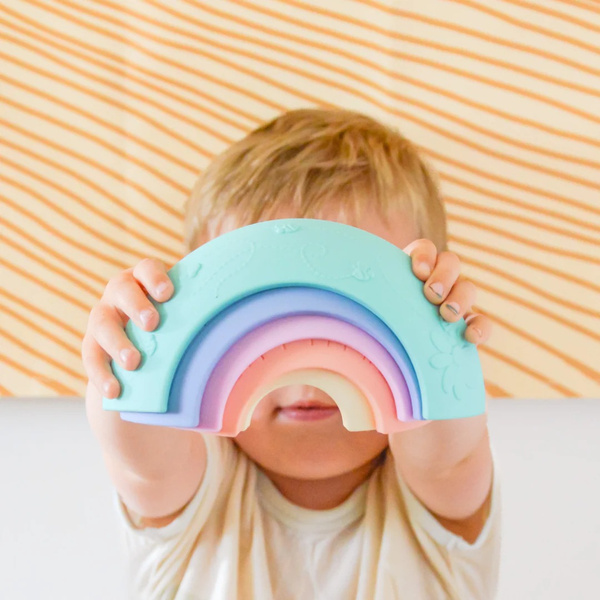 Pastelowa tęcza sensoryczna z pięciu elementów trzymana przez dziecko. Jellystone Designs Jellystone Tęcza sensoryczna Over the rainbow Pastel 5el. kolor pastelowy