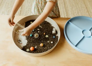 Okrągła tacka sensoryczna z czarnym piaskiem i kolorowymi kulkami oraz figurkami planet dla dziecka. Jellystone Designs Jellystone Zestaw sensoryczny Galaktyka wkład do tacki sensorycznej Play Tray