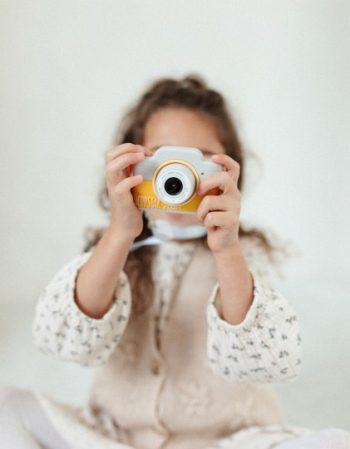 Dziecko trzymające żółto-biały aparat fotograficzny dla dzieci na białym tle. Hoppstar Aparat fotograficzny dla dzieci Expert Citron