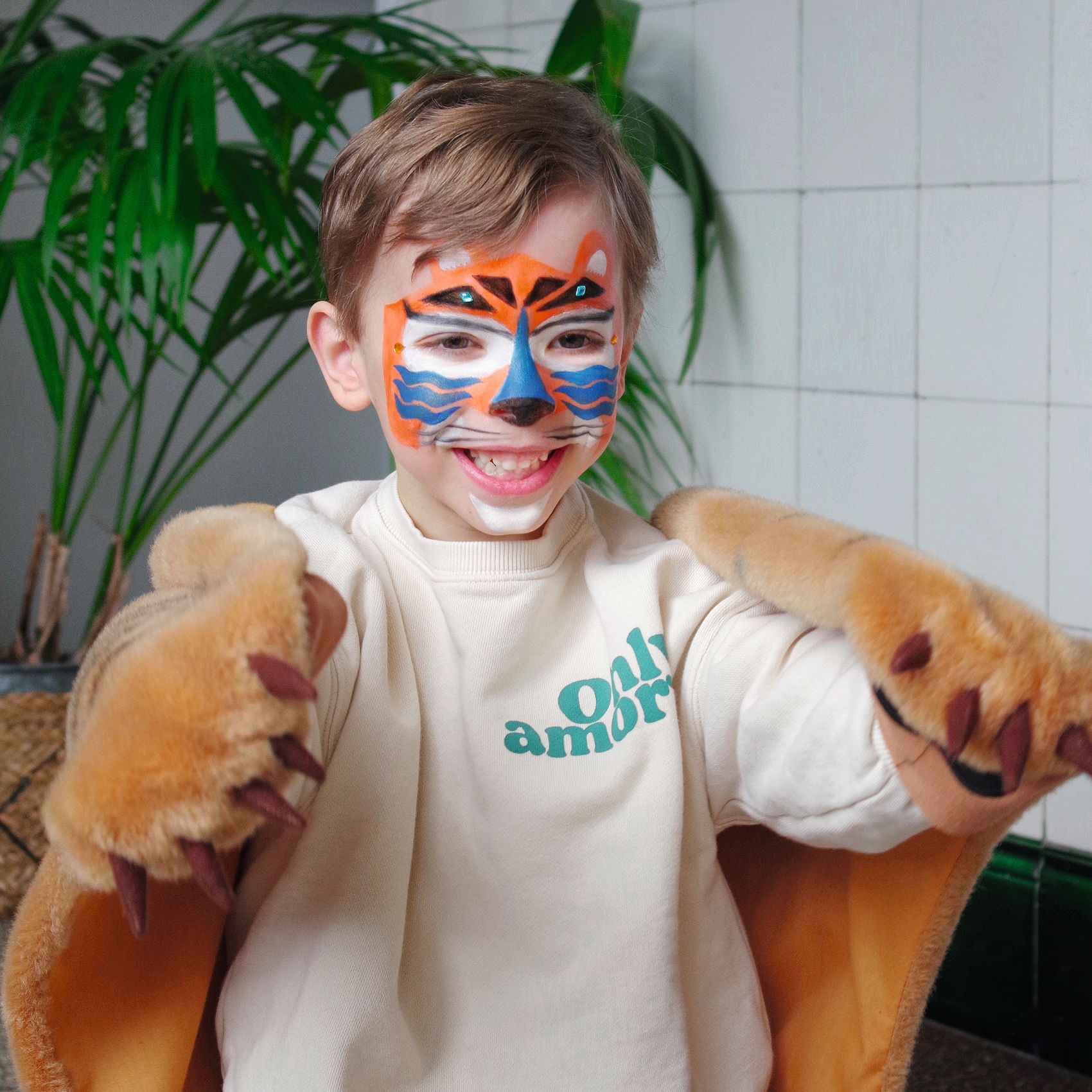 Chłopiec z pomalowaną twarzą na wzór pantery i pluszowe rękawice do przebrania dla dziecka. Djeco Farby do malow.twarzy z akcesor. PANTERA