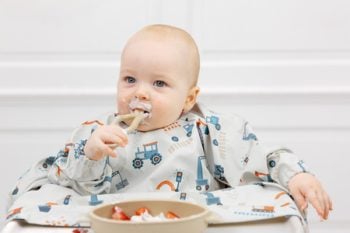 Niemowlę w wodoodpornym śliniaku z długim rękawem w wzór z pojazdami podczas jedzenia. BiBADO Wodoodporny śliniak z długim rękawem BLW Little Loader