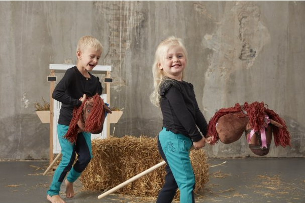 Dwoje dzieci bawiących się konikami na kiju z brązową głową i czerwoną grzywą na tle stodoły. byAstrup Koń na kiju Hobby Horse łaciaty z czarną grzywą