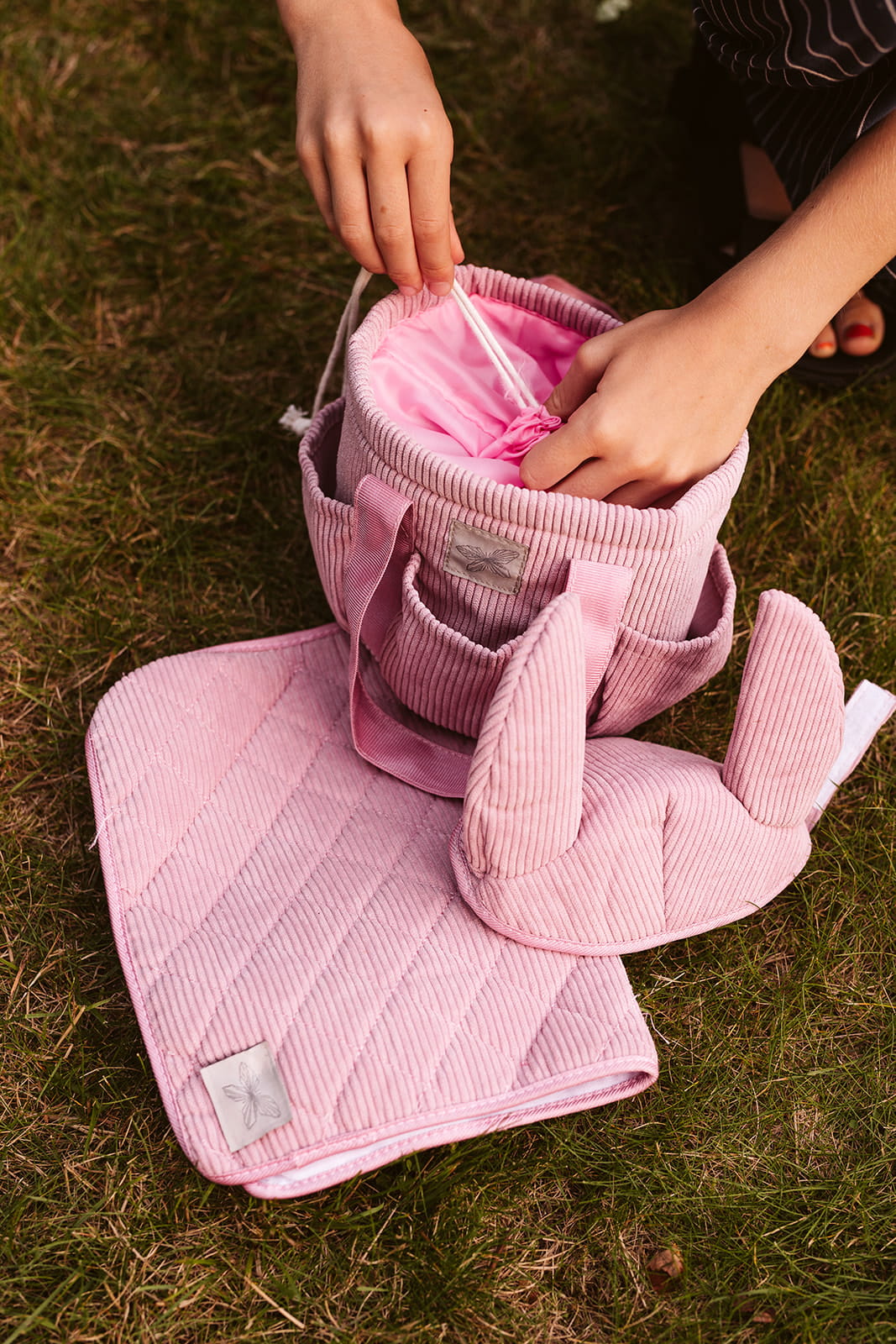 Różowa sztruksowa torba na akcesoria do Hobby Horse z uszami na trawie z różową podkładką i ochraniaczami dla dziecka. byAstrup Torba na akcesoria do Hobby Horse różowa sztruksowa