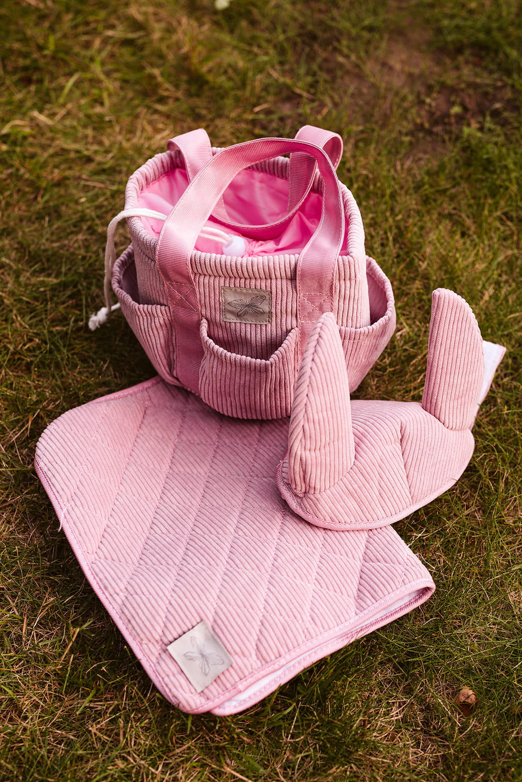Różowa sztruksowa torba na akcesoria do Hobby Horse z uchwytami oraz różowe pikowane nakładki na kopyta i podkładka pod siodło na trawie. byAstrup Torba na akcesoria do Hobby Horse różowa sztruksowa