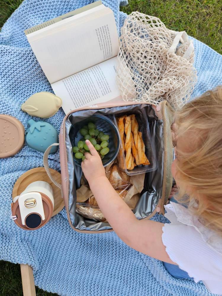 Torba termiczna na lunch beżowa z wnętrzem termoizolacyjnym dla dziecka na piknik z jedzeniem i owocami na niebieskim kocu. Vanilla Copenhagen Torba termiczna Cooler Bag NEO LILY Oak