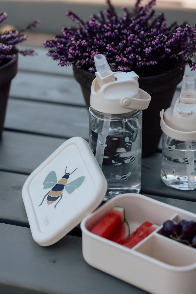 Przezroczysta butelka do picia z białym ustnikiem i słomką obok pojemnika na przekąski z motywem pszczoły dla dziecka. Vanilla Copenhagen Butelka do picia Tritan HONEYBEE 500 ml ze słomką