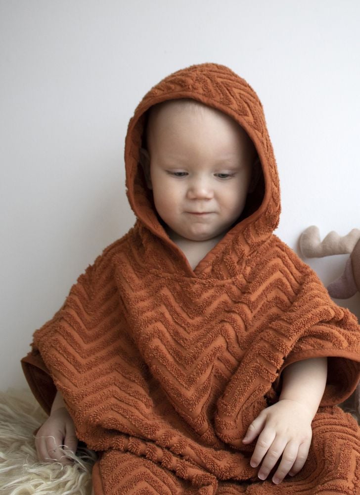 Niemowlę w kąpielowym ponczo z kapturem w kolorze rdzy z fakturą zygzakowego wzoru. Filibabba Poncho Zigzag Rust