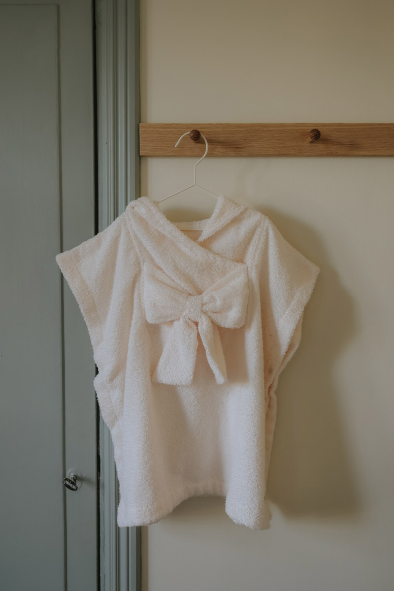 Kremowo białe ponczo kąpielowe z kapturem dla dziecka z miękkiego materiału zawieszone na wieszaku. Elodie Details Poncho kąpielowe creamy white