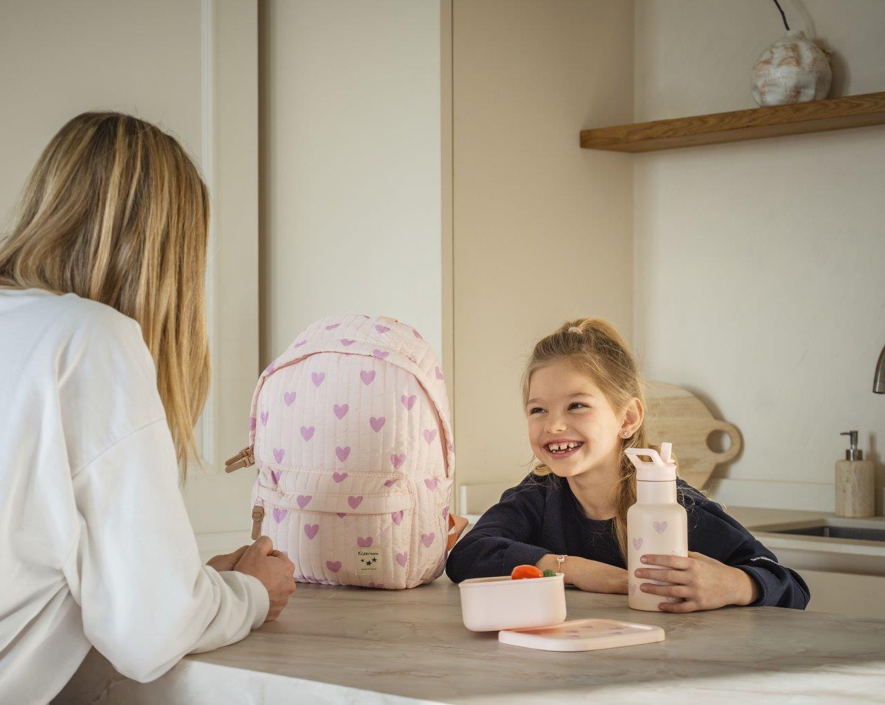 Różowy plecak dziecięcy z wzorem serc dla dziewczynki na stół w kuchni obok dziecka i dorosłej osoby. Kidzroom Plecak dla dzieci L Magical Heart pink