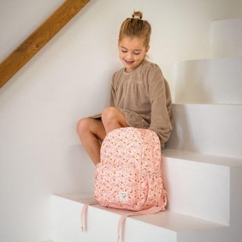 Różowy plecak dziecięcy w kwiaty na schodach obok siedzącej dziewczynki w beżowej sukience. Kidzroom Plecak dla dzieci L Memories Flowers Pink