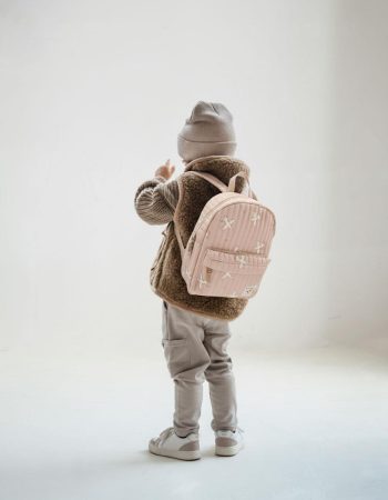 Dziecko w beżowej czapce i brązowej kamizelce nosi różowy plecak dziecięcy z wzorem dla dziecka. Kidzroom Plecak dla dzieci Wonderful Worlds Beige