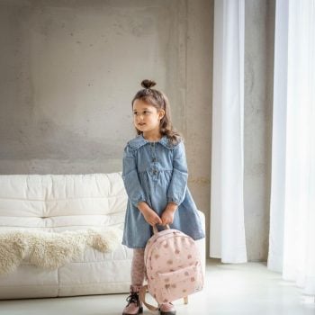 Dziewczynka w niebieskiej sukience trzymająca beżowy plecak dziecięcy z wzorem kwiatów w jasnym pokoju. Kidzroom Plecak dla dzieci Little Story Beige
