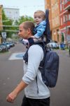 Mężczyzna noszący dziecko w nosidełku turystycznym z plecakiem na ulicy miasta. MiniMeis nosidełko G5 + plecak HERO Black Core ZESTAW