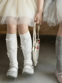 Białe podkolanówki z tiulowymi kokardkami dla dziecka na nogach dziewczynki. Fig&Pear Podkolanówki z kokardkami tiulowymi złamana biel