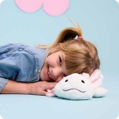 Dziewczynka leżąca na boku z pluszowym mini aksolotlem białym z różowymi wypustkami dla dziecka. Warmies Mini Axolotl Mini Aksolotl
