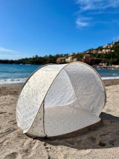 Biały namiot plażowy pop-up z siateczkowymi oknami na piasku przy morzu dla dziecka. Vanilla Copenhagen Namiot plażowy Pop-Up Tent Honeybee Happy UV50+