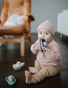 Niemowlę bawiące się zabawkami do kąpieli w kształcie łódek w pastelowych kolorach siedząc na podłodze. Mushie Zabawki do Kąpieli Łódki Orginal