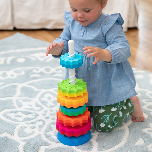Dziecko bawiące się kolorową zakręconą wieżą z klocków 3D na dywanie. Fat Brain Toy Co. Zakręcona Wieża SpinAgain