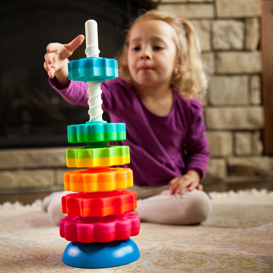 Dziecko układa kolorową zakręconą wieżę SpinAgain z klocków 3D na podłodze. Fat Brain Toy Co. Zakręcona Wieża SpinAgain