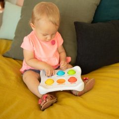 Niemowlę bawiące się kolorową zabawką sensoryczną z wypukłymi bąbelkami do naciskania na kanapie. Fat Brain Toy Co. Bąbelki Dimpl Duet