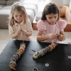 Dwie dziewczynki bawiące się koralikami do nawlekania na czarnym stole zabawka dla dzieci. Mushie Zabawka Koraliki do Nawlekania dla Dzieci