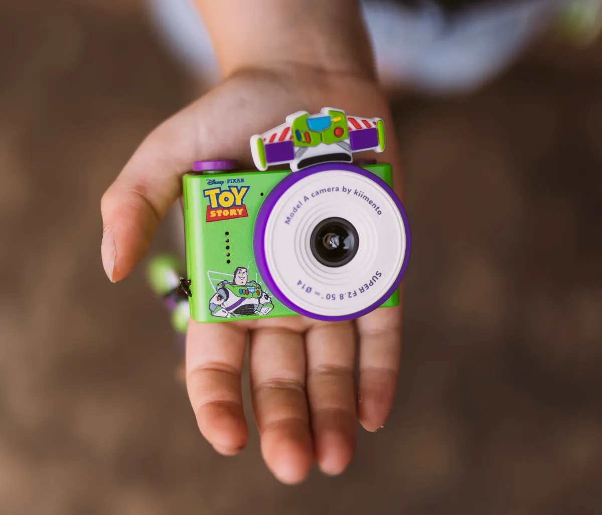 Mini aparat fotograficzny dla dzieci w kolorach zielonym i fioletowym z motywem Buzz Astral z Toy Story trzymany w dłoni. Kiimento Aparat Mini dla Dzieci Buzz Astral z Toy Story