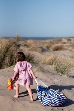 Dziecko na plaży ciągnące niebiesko-biały worek na zabawki i matę do zabawy w paski. Play&Go NOOMAD OUTDOOR Worek na Zabawki i Mata do Zabawy 2w1 Beac