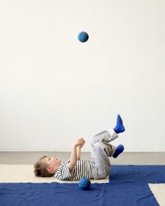 Dziecko leżące na plecach na niebieskim dywanie z piankową piłką w kolorze głęboki niebieski i jasny niebieski. MODU Foam Ball piłka piankowa deep blue / sky blue