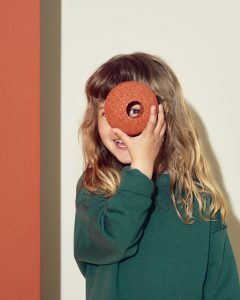 Dziecko trzyma pomarańczową piankową piłkę z otworem klocki piankowe dla dzieci. MODU Foam Ball piłka piankowa burnt orange / dusty green