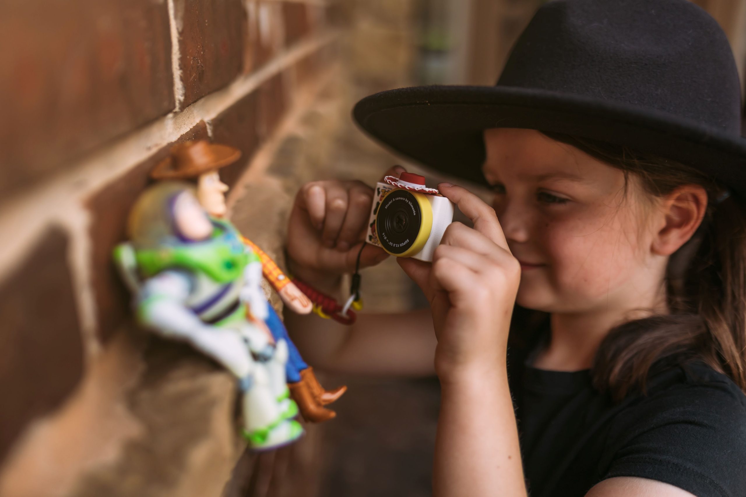 Dziecięcy aparat fotograficzny w kolorze żółtym z motywem kowbojki Jessie z Toy Story trzymany przez dziewczynkę w kapeluszu kowbojskim. Kiimento Aparat Mini dla Dzieci Kowbojka Jessie z Toy Story