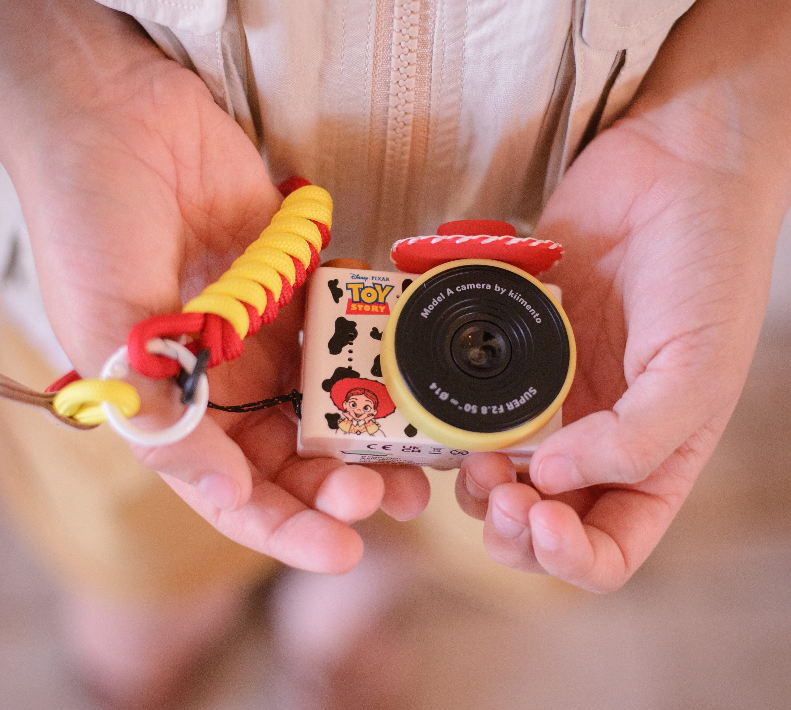 Mini aparat fotograficzny dla dzieci w kolorach czerwonym i żółtym z motywem kowbojki Jessie z Toy Story trzymany w dłoniach. Kiimento Aparat Mini dla Dzieci Kowbojka Jessie z Toy Story