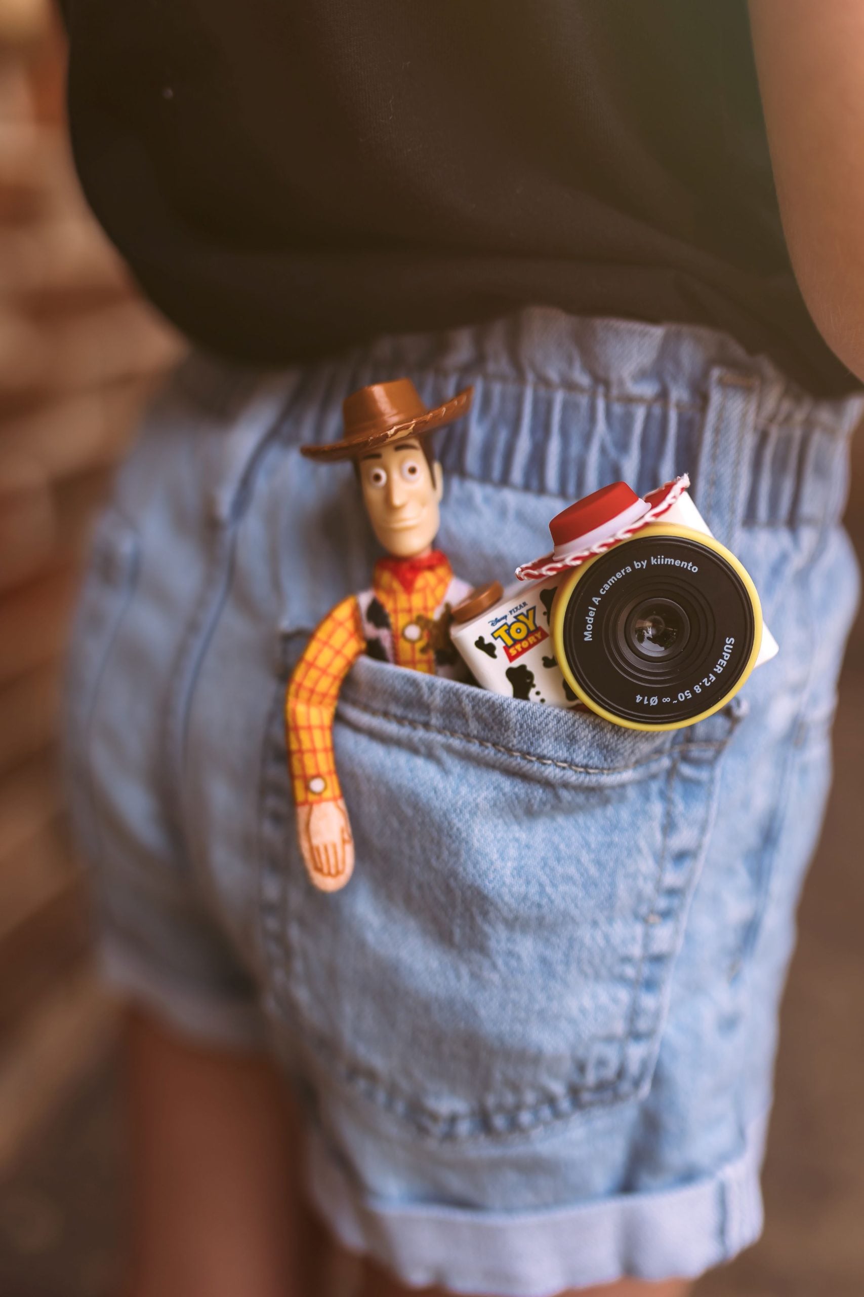 Dziecięcy aparat fotograficzny z motywem kowbojki Jessie z Toy Story w kieszeni jasnoniebieskich spodenek jeansowych. Kiimento Aparat Mini dla Dzieci Kowbojka Jessie z Toy Story