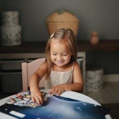 Dziewczynka bawiąca się naklejkami wielokrotnego użytku z motywem kosmosu na stole. Mushie Naklejki wielokrotnego użytku Kosmos
