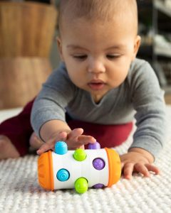 Niemowlę bawiące się kolorową zabawką do rozwijania zręczności Fat Brain Toy Co. Rolio Bobo Roller. Fat Brain Toy Co. Rolio Bobo Roller