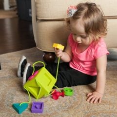 Dziecko bawiące się kolorowym sorterem kształtów z sznurkiem na dywanie. Fat Brain Toy Co. Sorter Kostka OombeeCube
