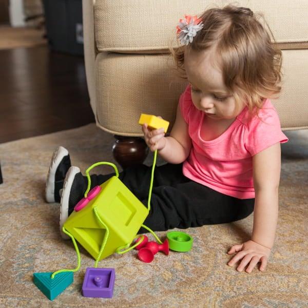Dziecko bawiące się kolorowym sorterem kształtów z sznurkiem na dywanie. Fat Brain Toy Co. Sorter Kostka OombeeCube