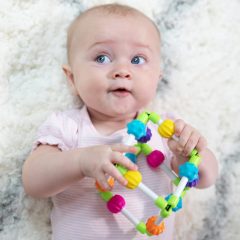 Niemowlę trzyma kolorową zabawkę sensoryczną sześcianik z elementami do chwytania i manipulacji. Fat Brain Toy Co. Sześcianik Quubi