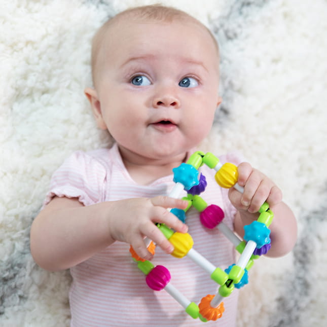 Niemowlę trzyma kolorową zabawkę sensoryczną sześcianik z elementami do chwytania i manipulacji. Fat Brain Toy Co. Sześcianik Quubi