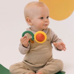 Niemowlę trzymające sensoryczną grzechotkę z kauczuku w zielonym i pomarańczowym kolorze. Oli & Carol Grzechotka Sensoryczna z Kauczuku Evolutive Capsule