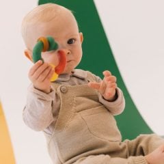 Niemowlę trzymające kolorowy gryzak z kauczuku dla dzieci marki Oli Carol na zielonym tle. Oli & Carol Gryzak Dla Niemowląt z Kauczuku Evolutive Capsule